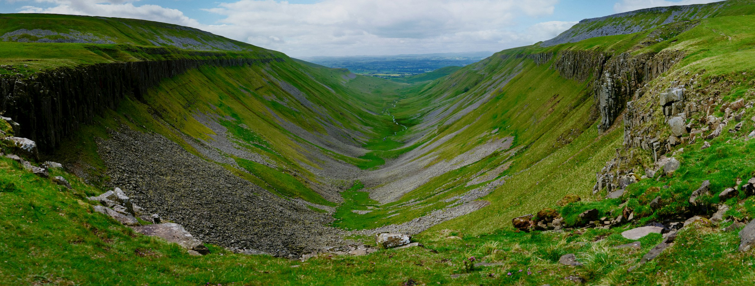 A valley carved into the earth with green grass and grey stones on either side.